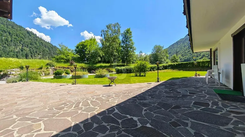 Große gepflasterte Terrasse mit angrenzendem Rasen und weitem Blick auf die umliegenden Berge.