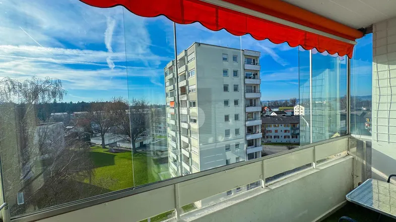 Verglaster Balkon mit Markise und weitem Blick auf umliegende Gebäude und die Landschaft.