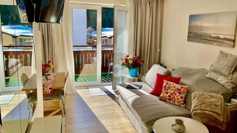 Helles Wohn- und Esszimmer mit Holzboden, gemütlichem Sofa und Zugang zu einem Balkon mit Bergblick.