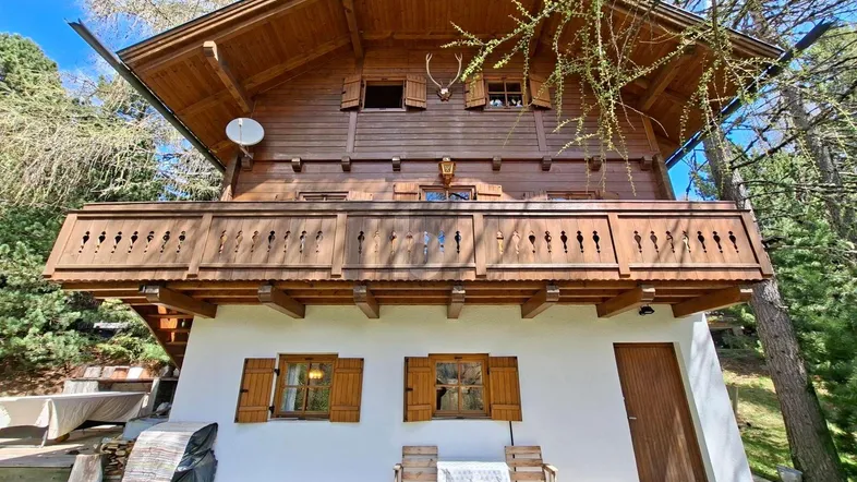 Traditionelles Holzchalet mit großem Holzbalkon und weißer Fassade im unteren Bereich.