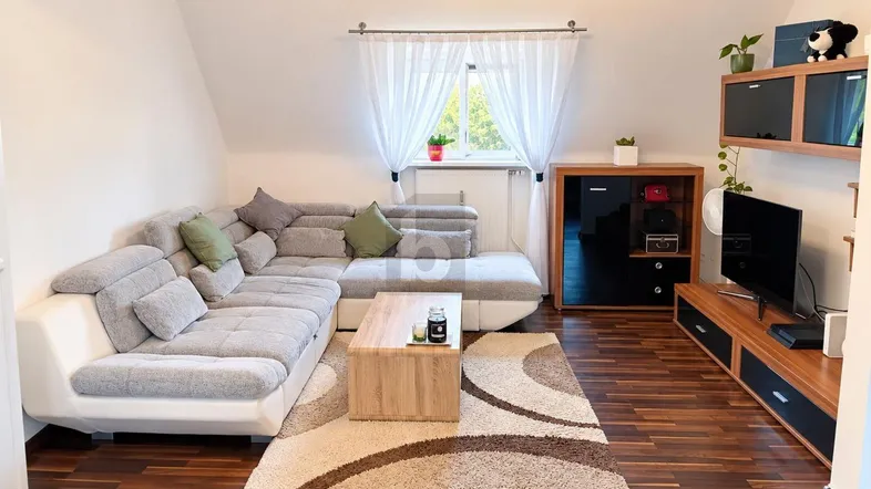 Gemütliches Wohnzimmer mit großem Ecksofa, Holzboden und Dachschrägenfenster.