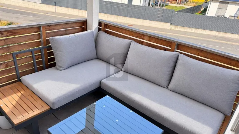 Gemütlicher Balkon mit moderner Lounge-Sitzgruppe und Blick auf Neubauten.