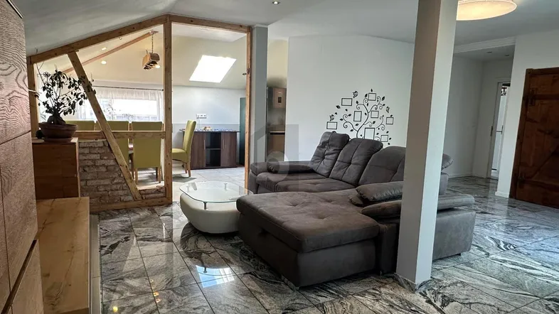 Offener Wohn- und Essbereich mit großem Sofa, gefliestem Boden und Blick auf den Essbereich mit Dachfenster.