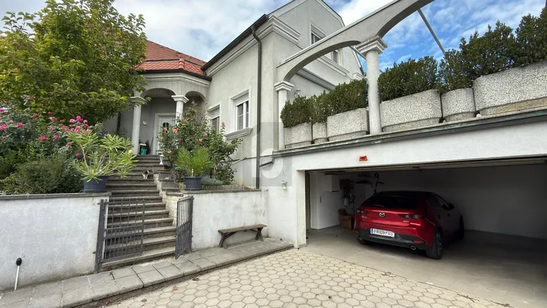Elegante Stadtvilla mit integrierter Garage, gepflegtem Vorgarten und einer Pergola über dem Eingangsbereich.