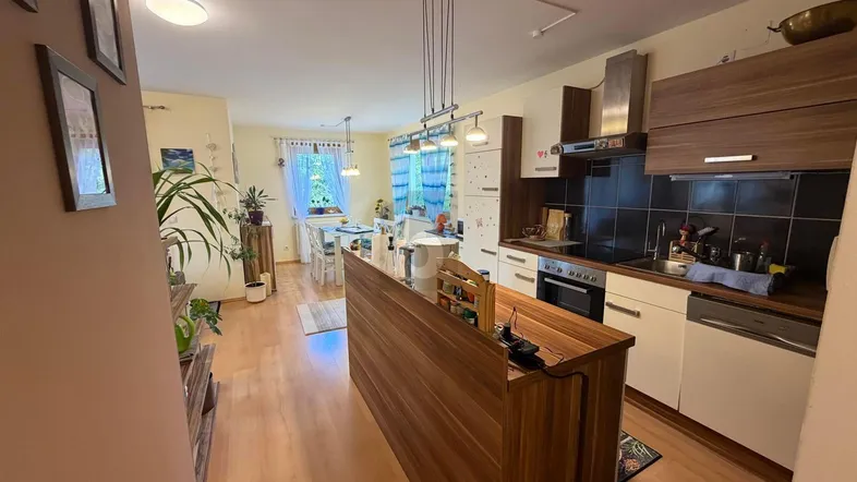 Moderne offene Küche mit Holzinsel, integrierten Geräten und Essbereich im Hintergrund.