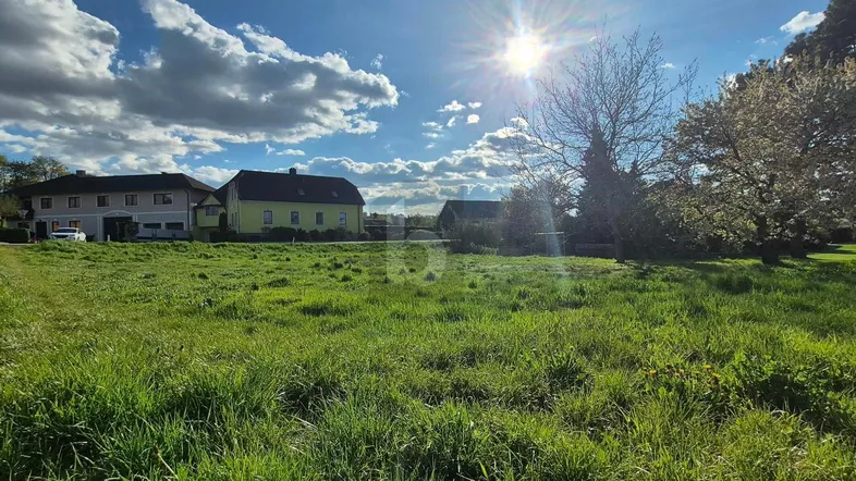 Sonniges Grundstück mit weitem Blick auf die umliegende Landschaft und Häuser im Hintergrund.
