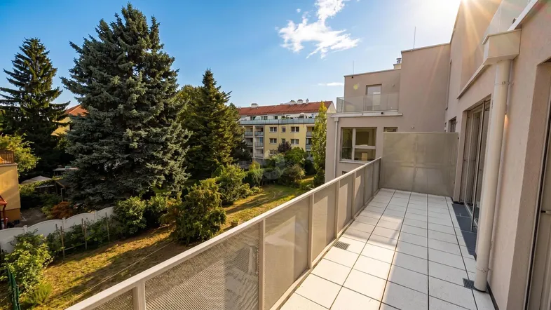 Sonniger Balkon mit Fliesenboden und Metallgeländer, der einen weiten Blick ins Grüne bietet.