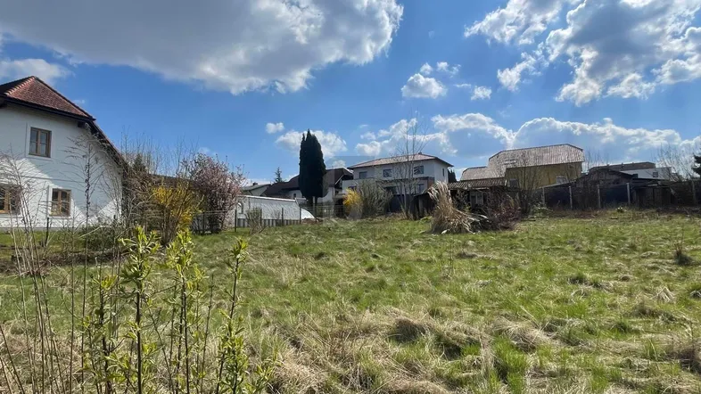 Weitläufiges Grundstück mit Grasfläche und Blick auf umliegende Wohnhäuser unter blauem Himmel.