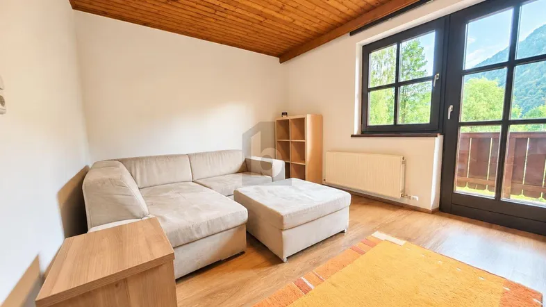 Helles Wohnzimmer mit gemütlichem Sofa, Holzdecke und Zugang zu einem Balkon mit Bergblick.