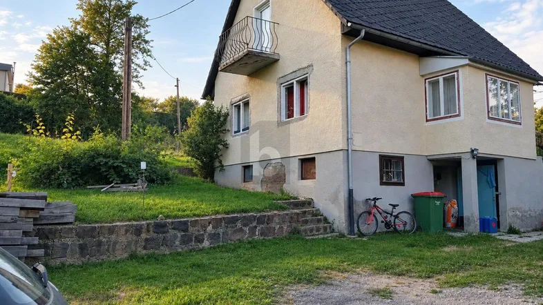 Einfamilienhaus mit heller Fassade, Satteldach und kleinem Balkon in ländlicher Umgebung.