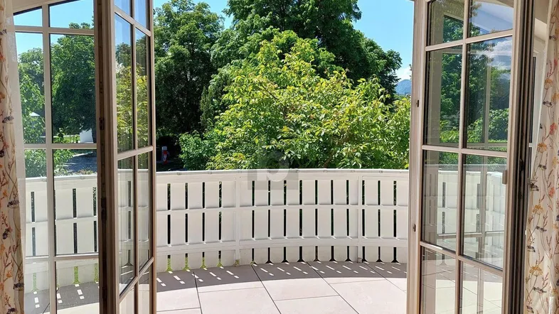 Helle Balkonansicht mit geöffneten Fenstertüren und weitem Blick ins Grüne.