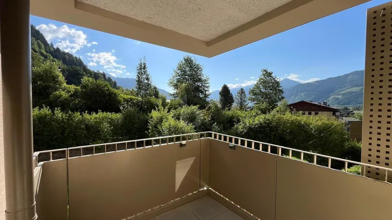 Geräumiger Balkon mit Fliesenboden und weitem Blick auf die umliegende Berglandschaft und viel Grün.