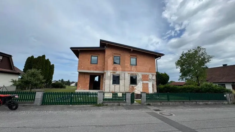 Rohbau eines Einfamilienhauses mit Ziegelwänden und grüner Umzäunung, bereit für den weiteren Ausbau.