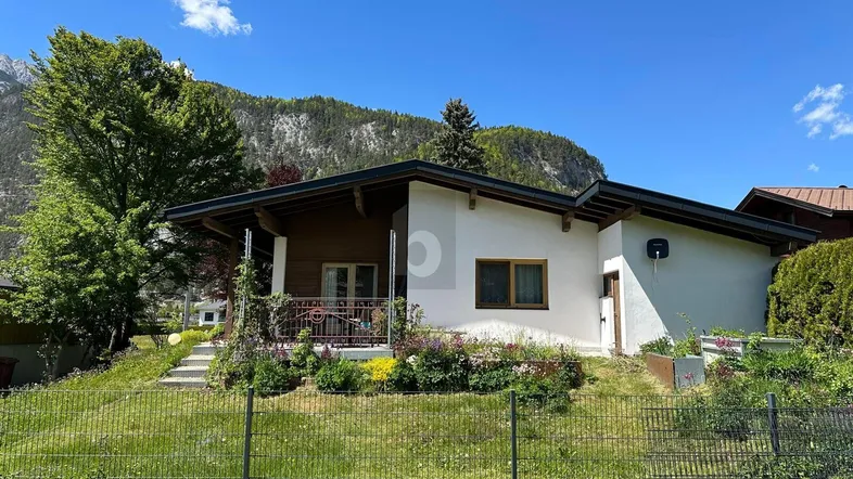 Modernes Haus mit Garten, grüner Umgebung und beeindruckendem Bergblick unter blauem Himmel.