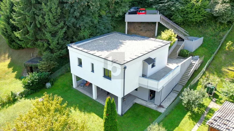 Moderne Architektur mit Flachdach und Hanglage, umgeben von viel Grün und Parkmöglichkeiten.