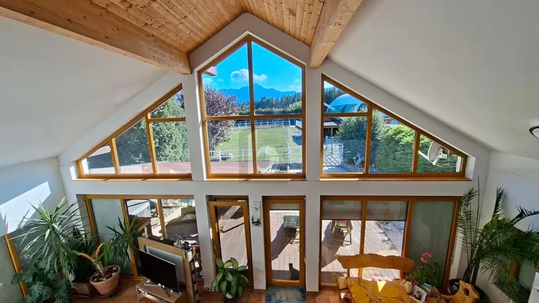 Heller Wohnbereich mit hohen Decken, großen Fenstern und Bergblick, ausgestattet mit rustikalen Holzmöbeln.