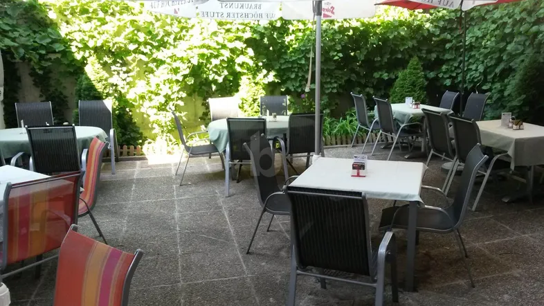 Gemütlicher Außenbereich mit Tischen, Stühlen und Sonnenschirmen, umgeben von üppigem Grün.