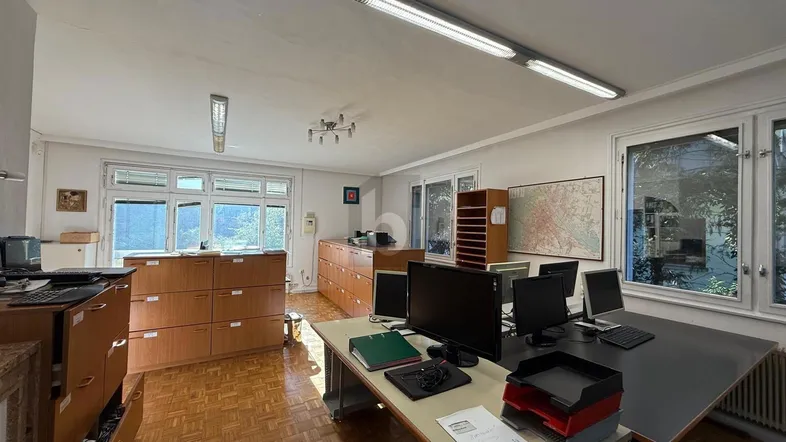 Geräumiges Büro mit mehreren Arbeitsplätzen, Parkettboden und großen Fenstern, die viel Tageslicht hereinlassen.