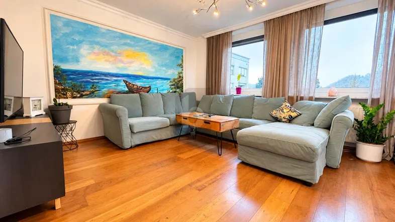 Helles Wohnzimmer mit großem Ecksofa, Holzboden und einem farbenfrohen Wandgemälde.