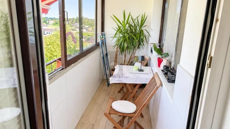 Helles, verglastes Balkonzimmer mit Sitzgelegenheiten und Blick ins Grüne.
