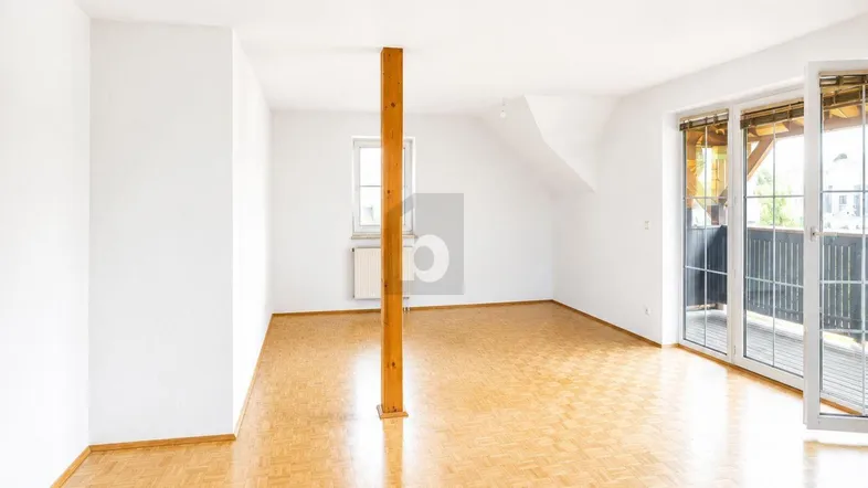 Heller, leerer Raum mit Parkettboden, Holzbalken und Zugang zu einem Balkon.
