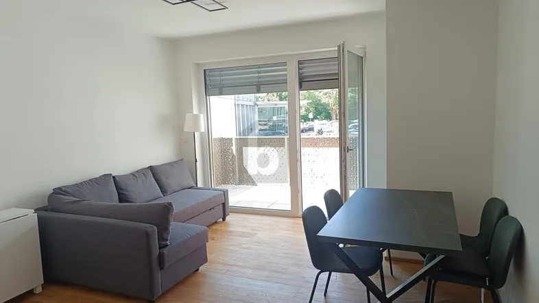 Helles Wohn- und Esszimmer mit Holzboden, modernem Sofa und Zugang zu einem Außenbereich.