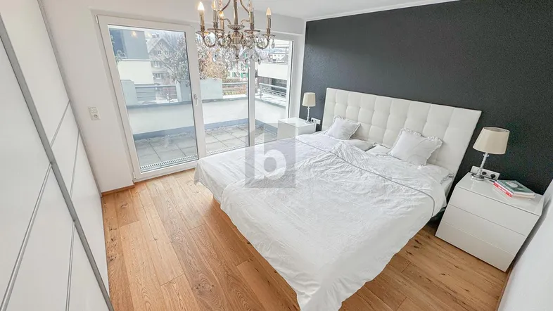 Helles Schlafzimmer mit Holzboden, großem Bett, dunkler Akzentwand und Zugang zu einer Terrasse.