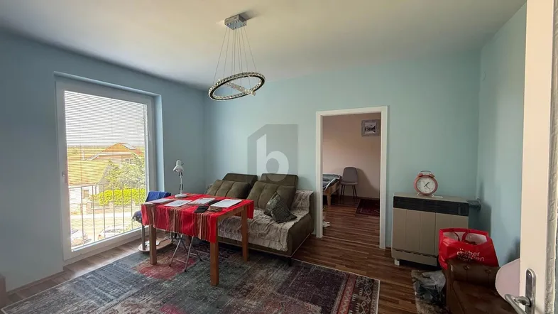 Helles Wohnzimmer mit hellblauen Wänden, Holzboden und Zugang zu einem weiteren Raum.