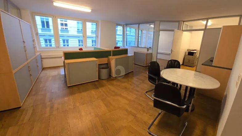 Geräumiges Büro mit mehreren Arbeitsplätzen, Holzparkettboden und großen Fenstern für viel Tageslicht.