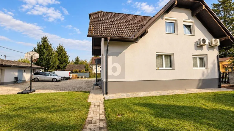 Ansicht des Hauses von der Seite mit Rasenfläche, Einfahrt und Nebengebäude unter blauem Himmel.
