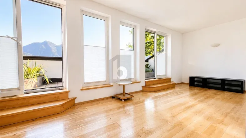 Helles Wohnzimmer mit Holzboden und großen Fenstern, die einen Bergblick bieten und Zugang zu einem Balkon ermöglichen.