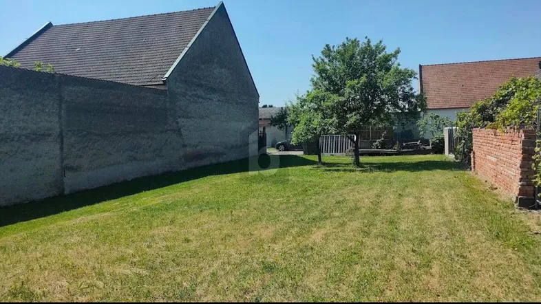 Großer Gartenbereich mit Rasenfläche und Bäumen, umgeben von Mauern unter blauem Himmel.