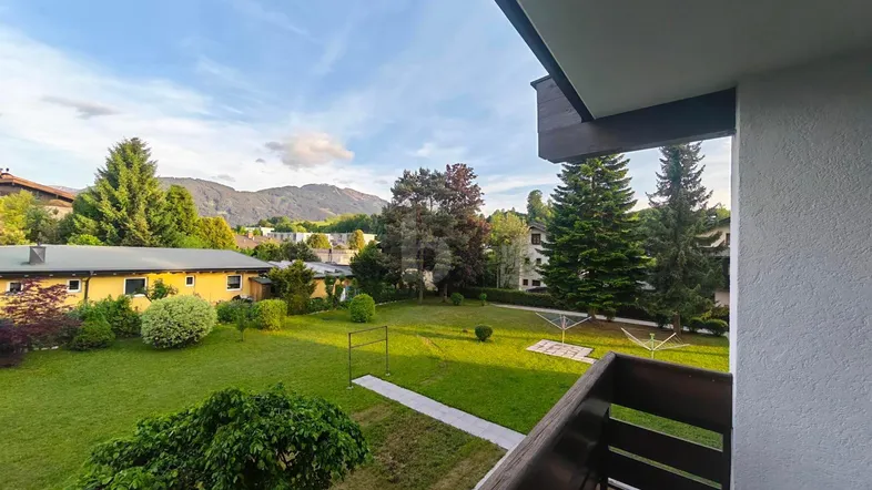Blick vom Balkon auf einen gepflegten Garten mit Rasenfläche und majestätischem Bergpanorama im Hintergrund.