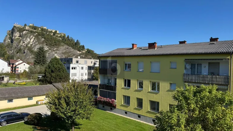 Gebäudeansicht mit grüner Umgebung und Blick auf eine historische Burg auf dem Berg.