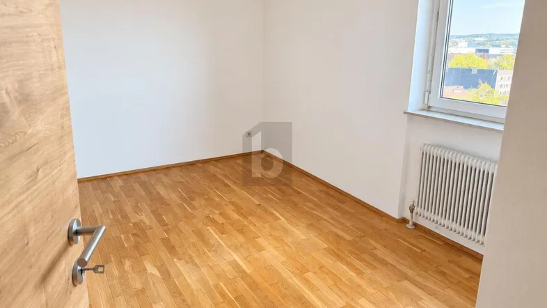 Helles Zimmer mit Parkettboden und Fenster, das einen Blick nach draußen bietet.