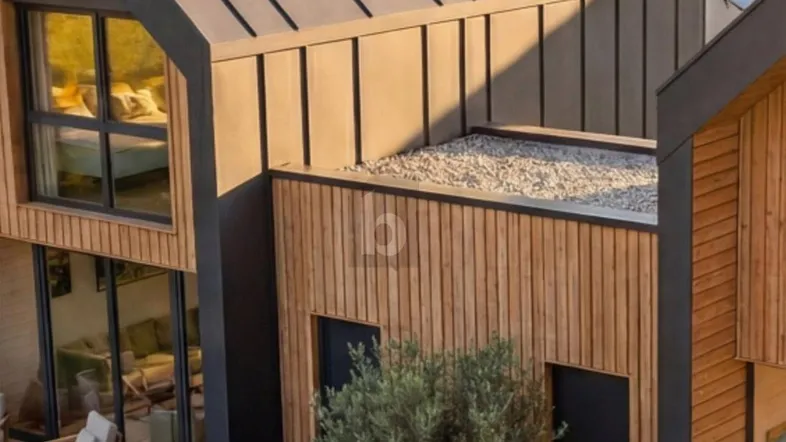 Moderne Architektur mit Holzfassade, großen Fenstern und einer kleinen Terrasse mit Sitzgelegenheiten.