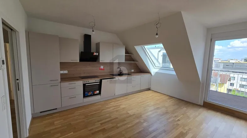 Moderne Einbauküche in einem hellen Dachgeschossraum mit Holzboden, Schrägdachfenster und Zugang zu einem Balkon.