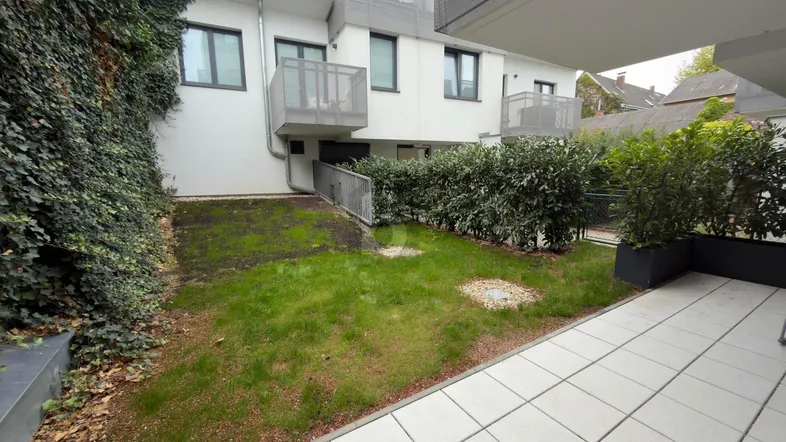 Gepflegter Gartenbereich mit Rasenfläche und einer kleinen Terrasse vor einem modernen Gebäude.