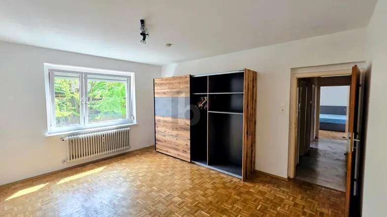 Helles Schlafzimmer mit Fischgrätparkettboden, großem Fenster und modernem Kleiderschrank.