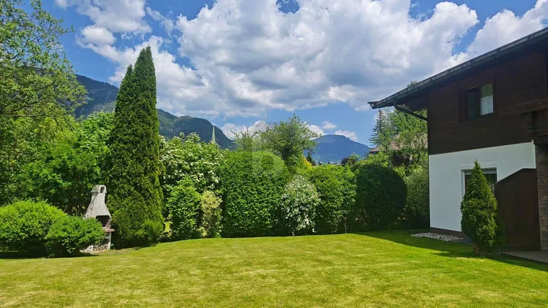 Gepflegter Rasenbereich mit Grillstelle und Blick auf die umliegende Berglandschaft unter blauem Himmel.