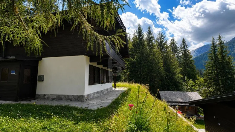 Traditionelles Haus in alpiner Umgebung mit dunkler Holzfassade und weißem Sockel.