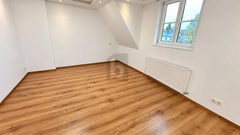 Helles Zimmer mit Laminatboden, Dachschräge und Fenster mit Blick nach draußen.