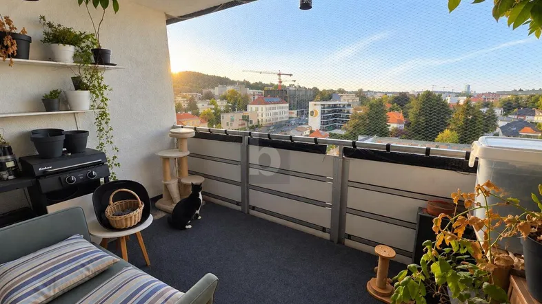 Gemütlicher Balkon mit Sitzgelegenheiten, Pflanzen und Stadtblick bei Sonnenuntergang.
