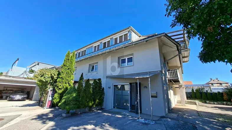 Mehrstöckiges Gebäude mit moderner Fassade, Balkonen und einem Carport im Freien.