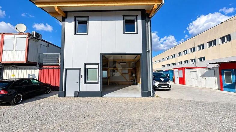 Modernes zweistöckiges Gebäude mit großer Garageneinfahrt und Holzüberdachung auf einem Schotterparkplatz.
