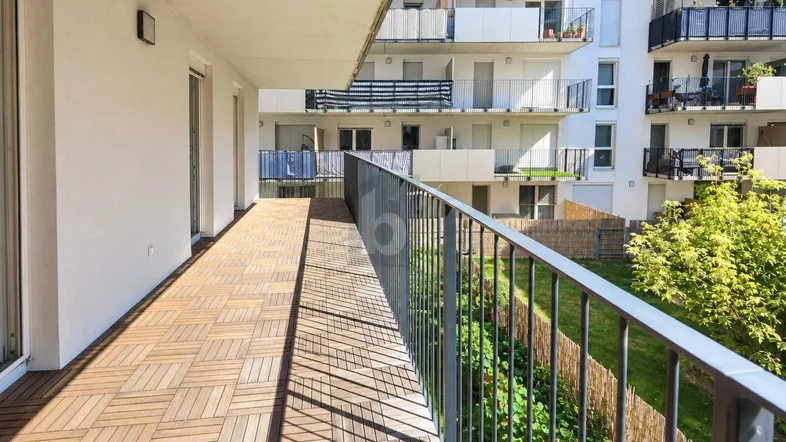 Langer Balkon mit Holzbodenfliesen und Blick auf die umliegenden Gebäude und Grünflächen.