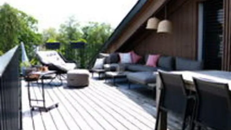 Geräumige Dachterrasse mit Holzdeck, Lounge-Möbeln und Essbereich unter schrägem Dach.