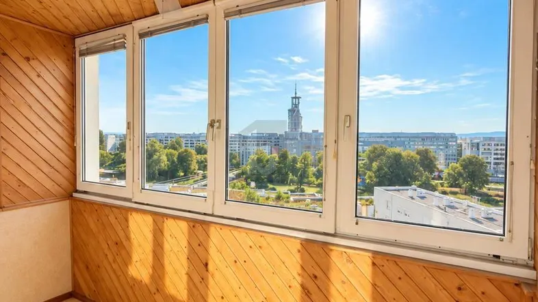 Verglaster Balkon mit Holzverkleidung, Deckenventilator und weitem Blick über die Stadt.