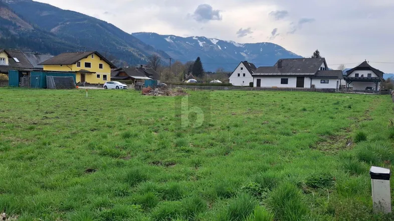 Weitläufiges Grundstück mit grüner Wiese, umgeben von Häusern und einer beeindruckenden Bergkulisse.