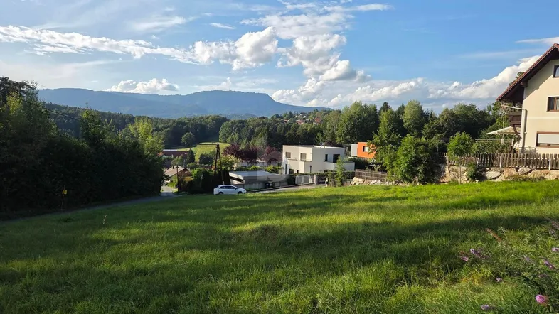 Weitläufige Grünfläche mit Blick auf die umliegende Landschaft und Berge unter blauem Himmel.